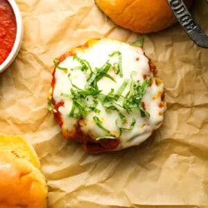 a bottom bun topped with a cheesy chicken burger patty and shredded basil.