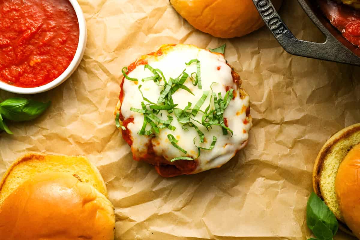 a bottom bun topped with a cheesy chicken burger patty and shredded basil.