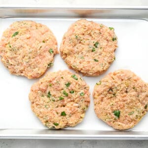 4 raw ground chicken burger patties on a baking sheet.