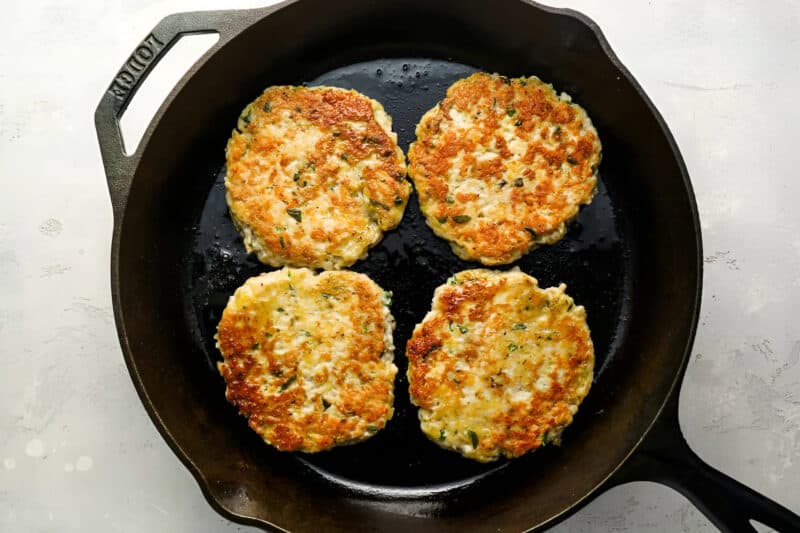 4 cooked ground chicken burger patties in a cast iron pan.