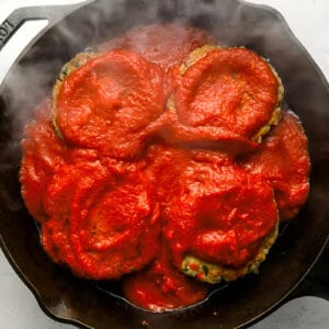 four chicken burger patties topped with marinara sauce in a cast iron pan.