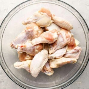 raw chicken wings in a glass bowl tossed with oil.