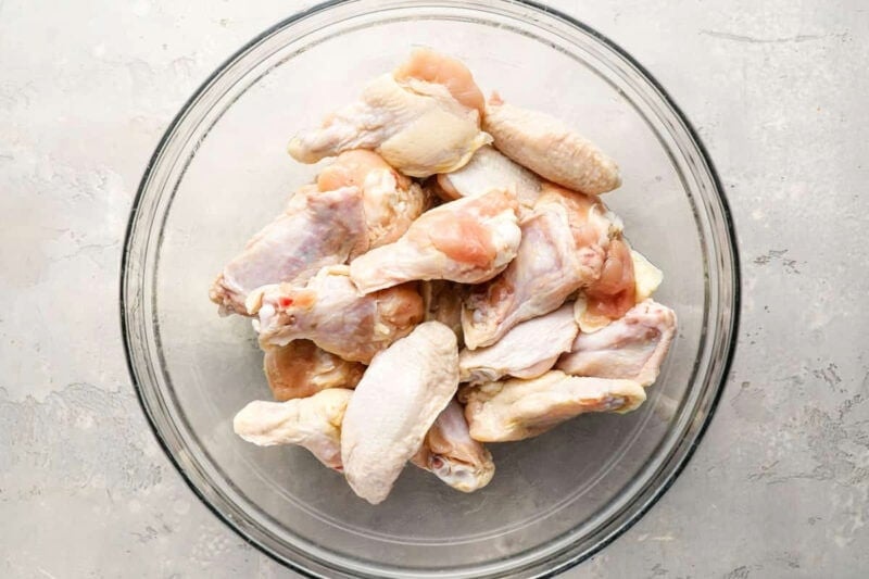 raw chicken wings in a glass bowl tossed with oil.