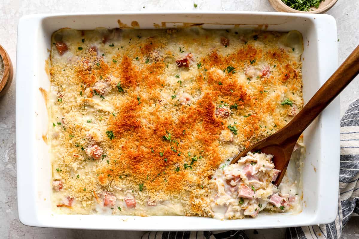overhead view of a baked chicken cordon bleu casserole with a wooden spoon.