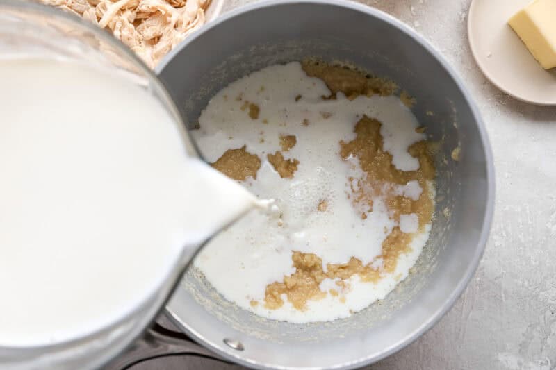 pouring milk over a roux in a saucepan.
