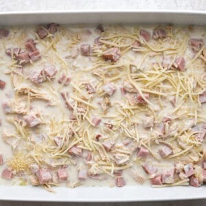 layers of shredded chicken, cubed ham, white sauce, and cheese in a casserole dish.