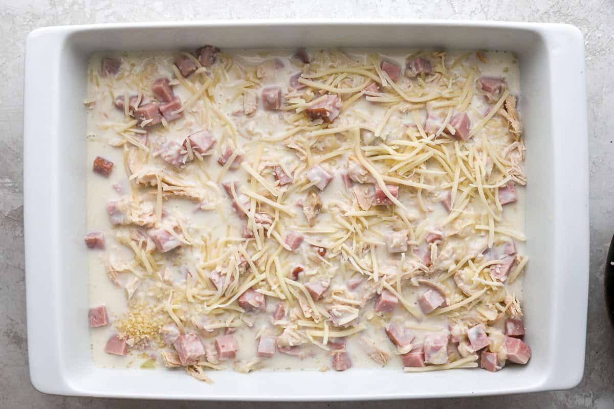 layers of shredded chicken, cubed ham, white sauce, and cheese in a casserole dish.