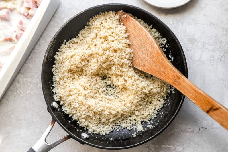 toasting breadcrumbs in a skillet with a wooden spoon.