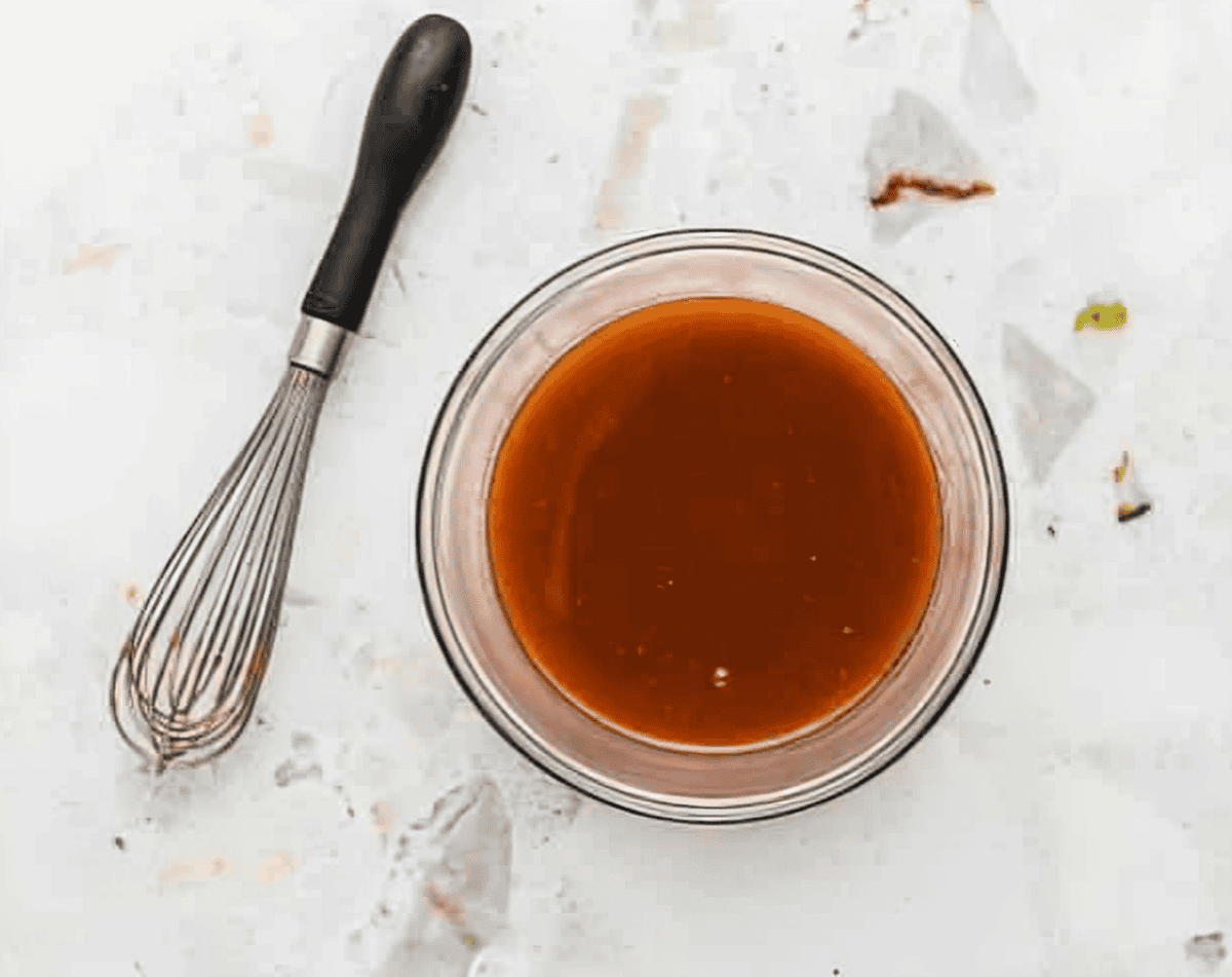 A whisk sitting next to a bowl of buffalo sauce.