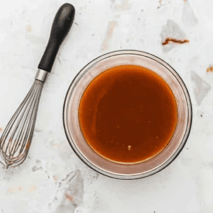 A whisk sitting next to a bowl of buffalo sauce.