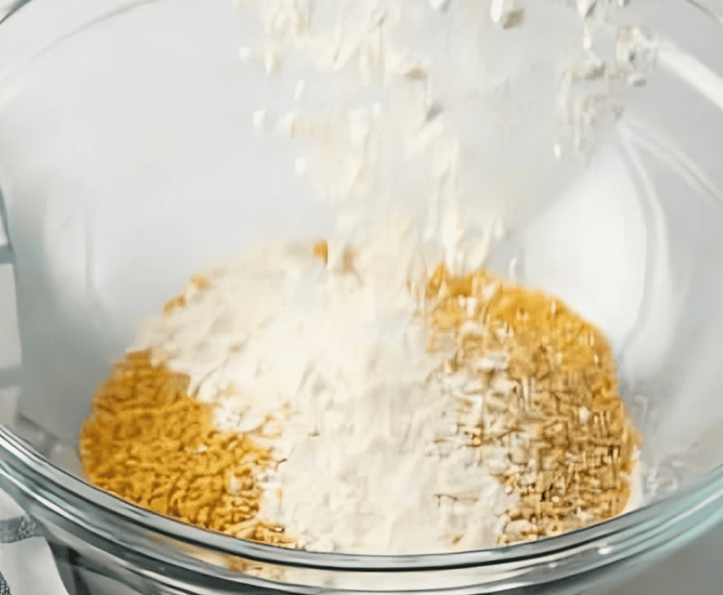 Adding flour into a bowl with crushed cornflakes.