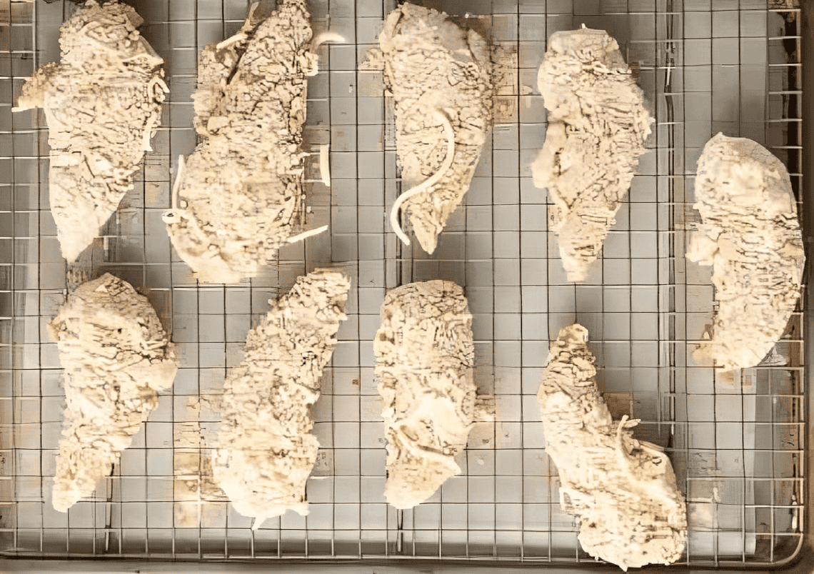 Uncooked chicken strips coated in flour breading mixture, lined up on a baking tray.