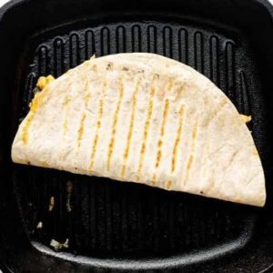 Folded quesadilla cooking on a grill pan.