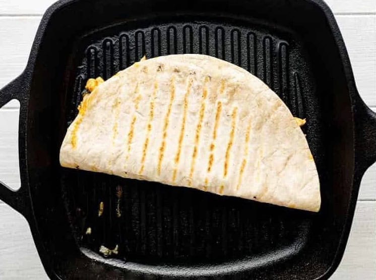 Folded quesadilla cooking on a grill pan.