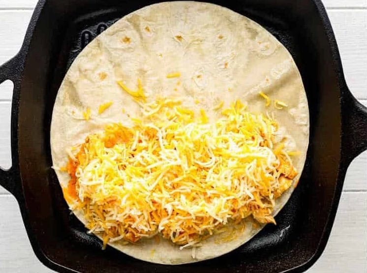 Buffalo chicken and shredded cheese on half of a tortilla.