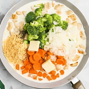 Cream, broccoli, carrots, chicken, butter, and cheese in a skillet.