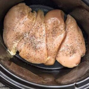 4 raw chicken breasts lined up in a Crockpot.