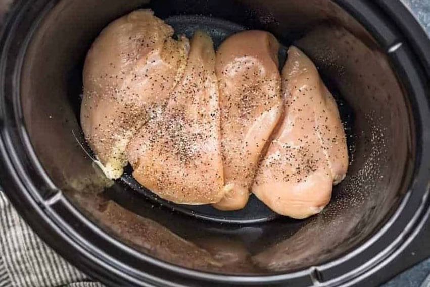 4 raw chicken breasts lined up in a Crockpot.