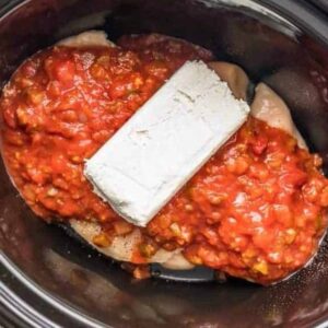 Chicken breasts, salsa, and cream cheese in a slow cooker.