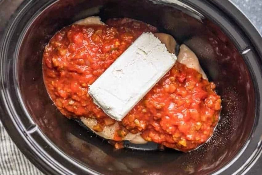 Chicken breasts, salsa, and cream cheese in a slow cooker.