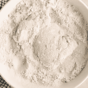 Chicken thigh dredged in a bowl of flour.