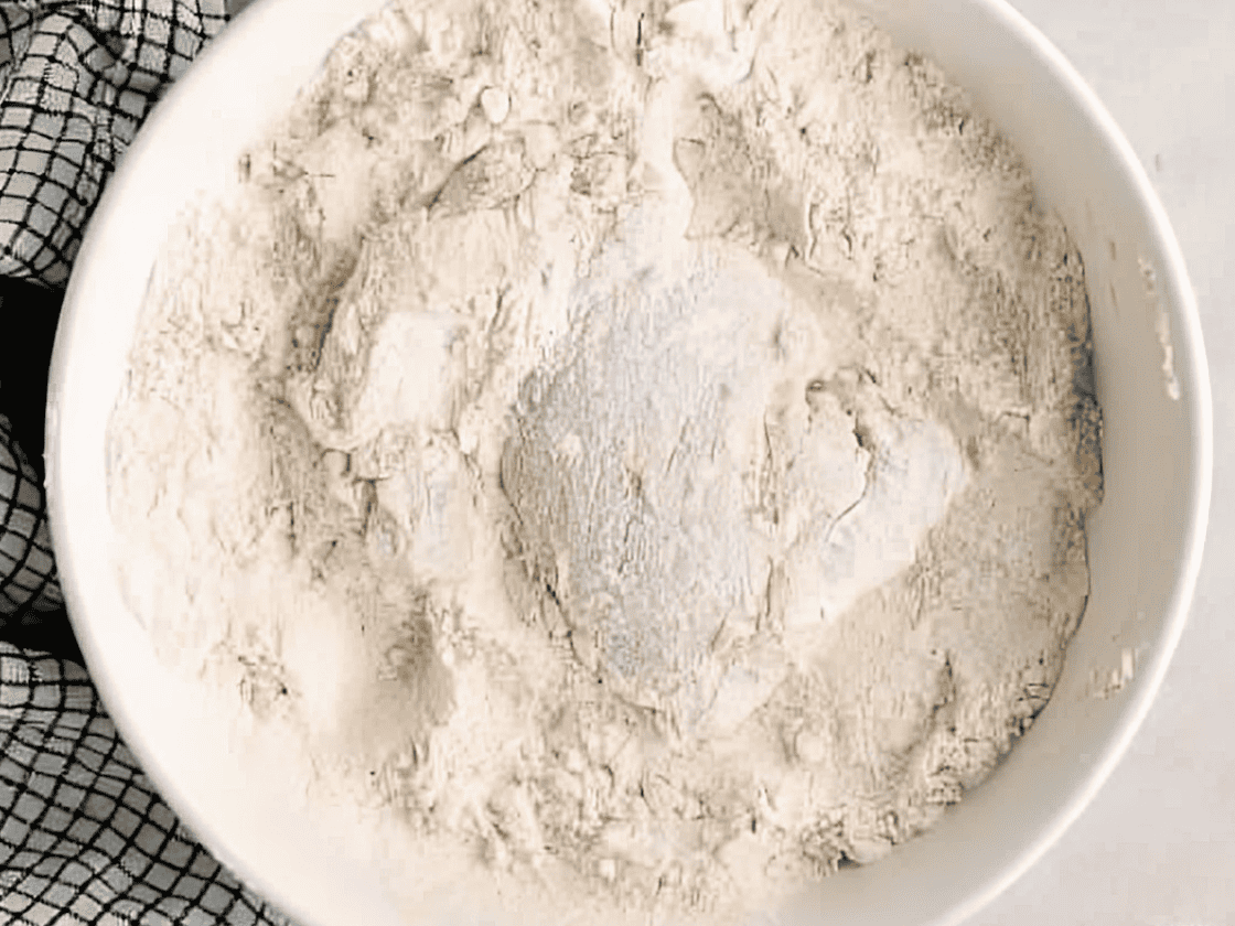 Chicken thigh dredged in a bowl of flour.