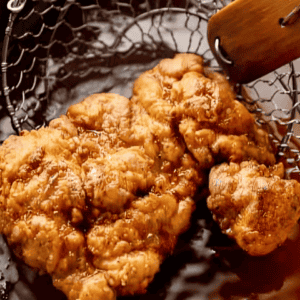 Frying pieces of chicken in a pot of oil.