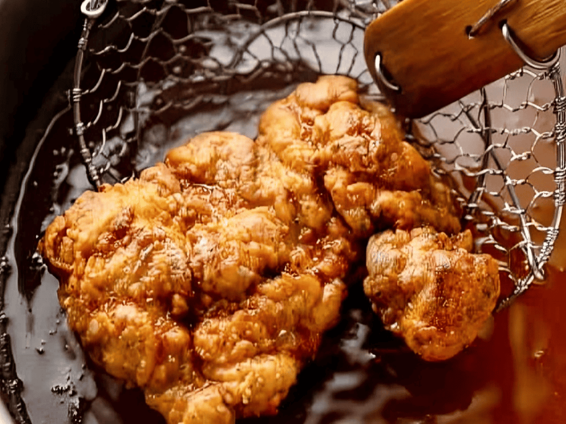 Frying pieces of chicken in a pot of oil.