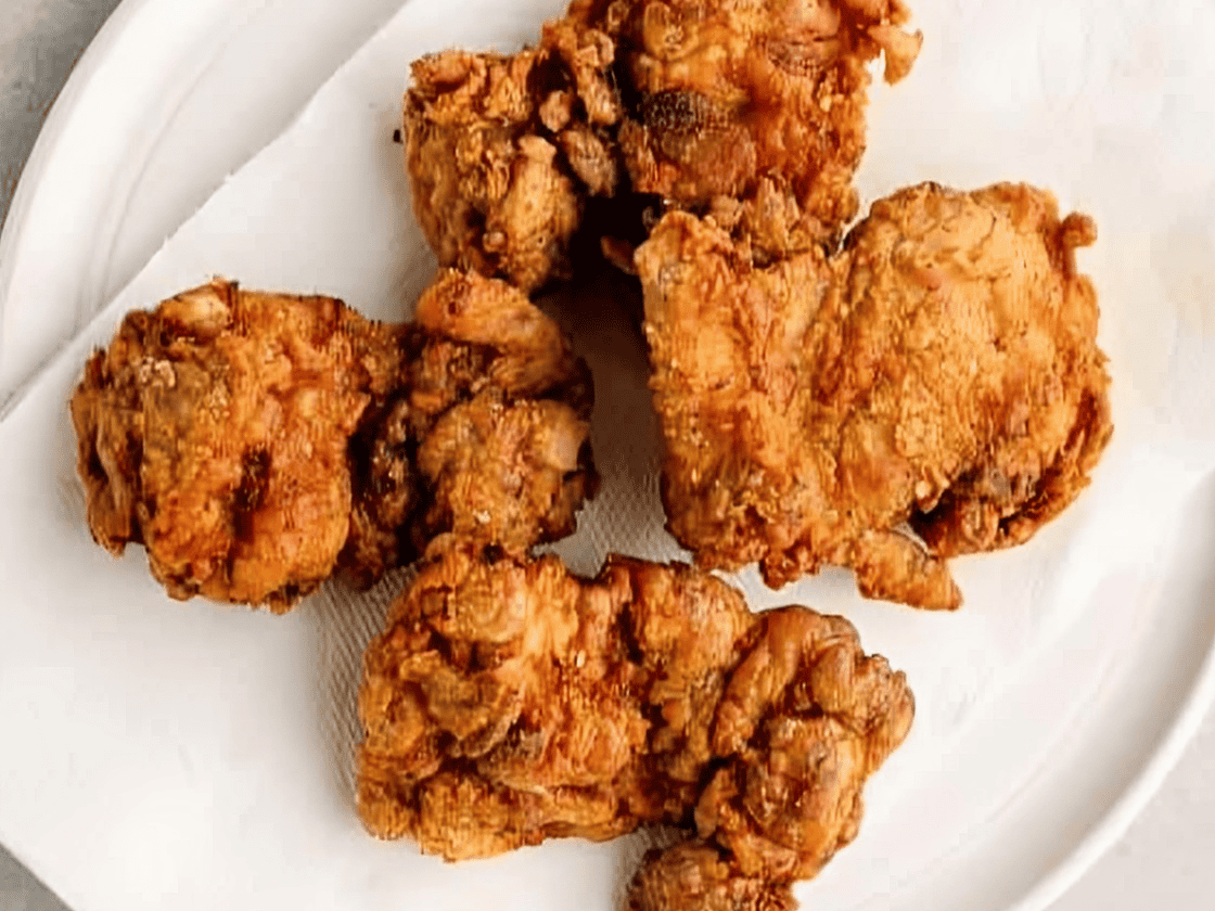 Fried chicken thighs on a paper towel lined plate.