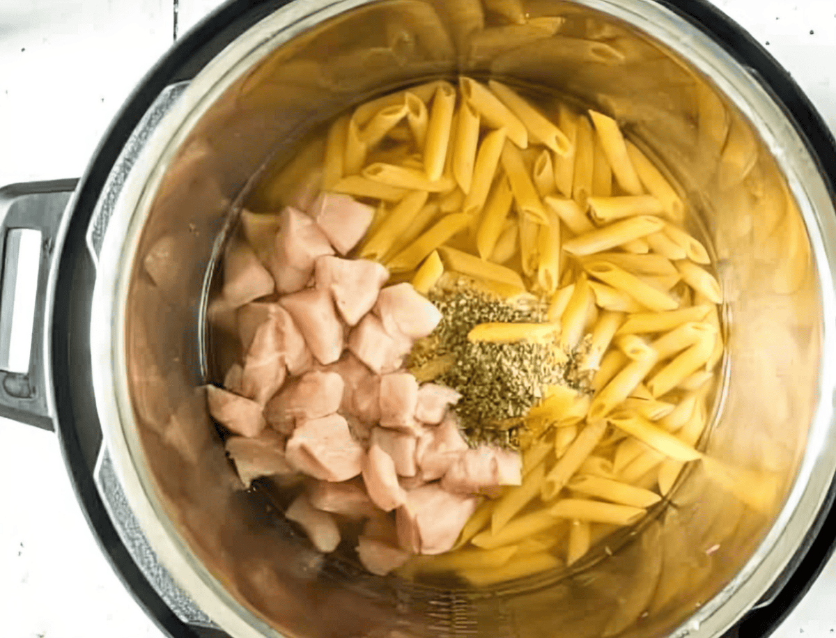 Penne pasta, seasonings, and bites of chicken in an Instant Pot.