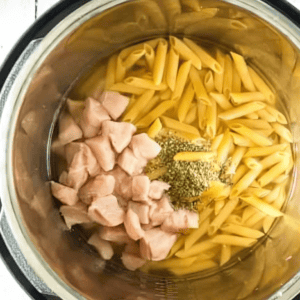 Penne pasta, seasonings, and bites of chicken in an Instant Pot.