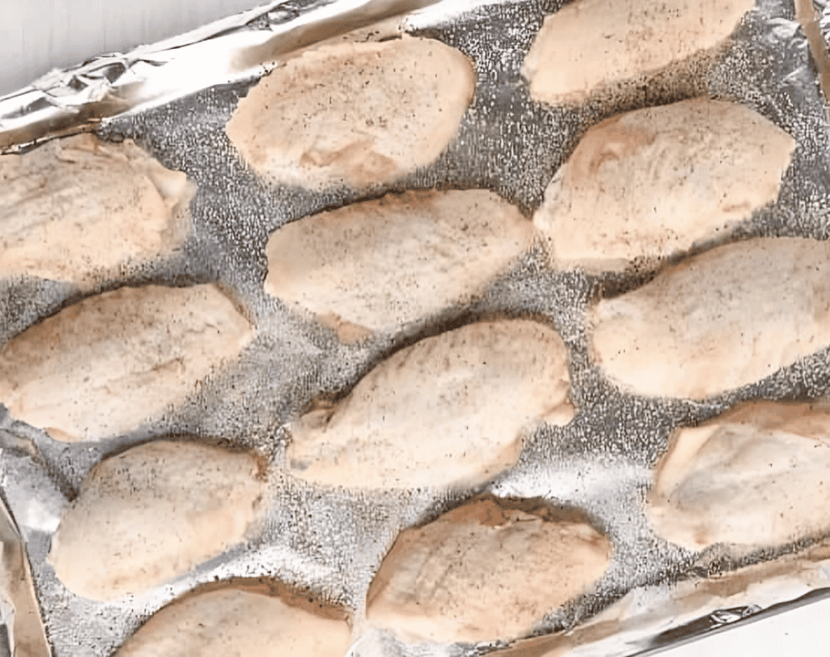 Uncooked chicken wings lined up on a baking tray covered with aluminum foil.