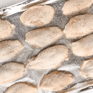 Uncooked chicken wings lined up on a baking tray covered with aluminum foil.