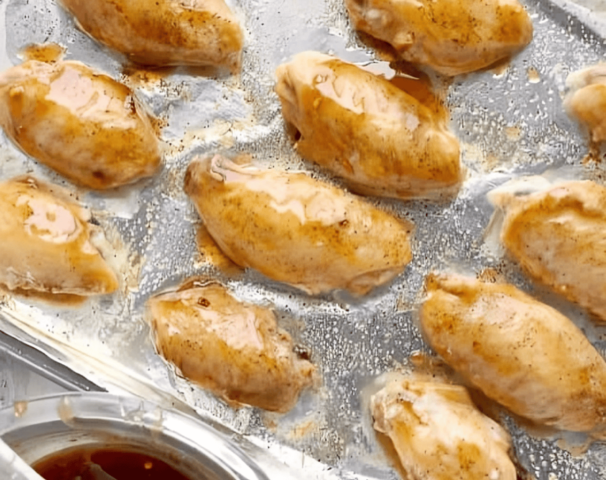 Chicken wings coated with sweet chili sauce, on a baking tray.