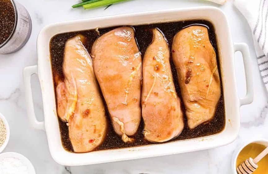 Chicken breasts sitting in a dish of teriyaki marinade.