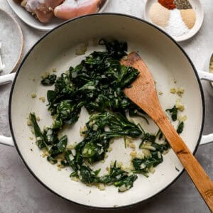 wilted spinach in a pan with a wooden spatula.