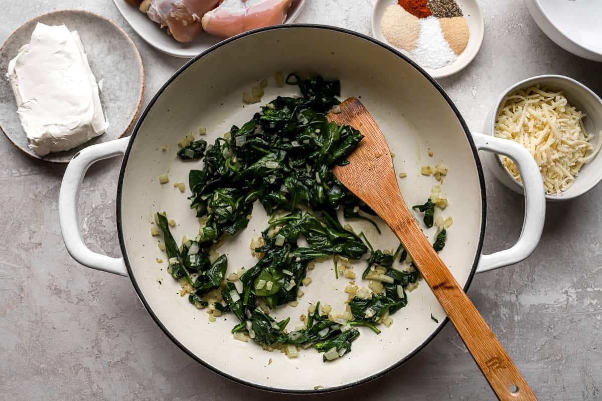 wilted spinach in a pan with a wooden spatula.