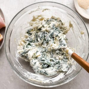 cheesy spinach filling in a glass bowl with a rubber spatula.