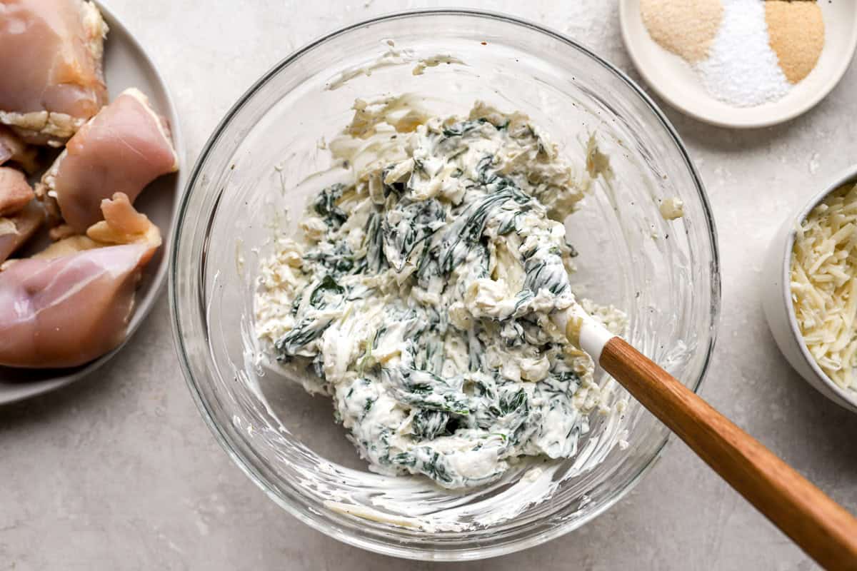 cheesy spinach filling in a glass bowl with a rubber spatula.