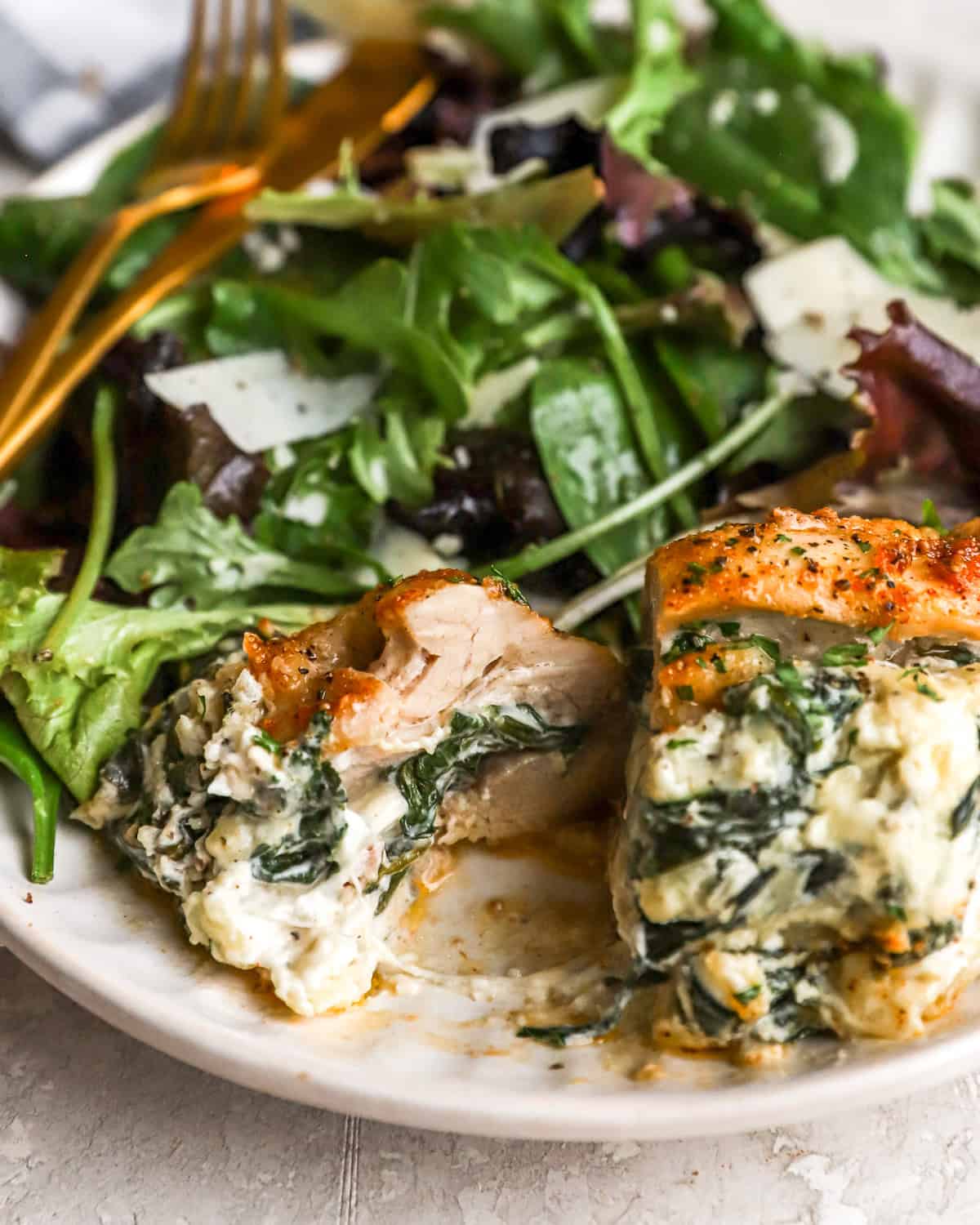 a serving of spinach and cheese stuffed chicken thighs on a plate with a salad.