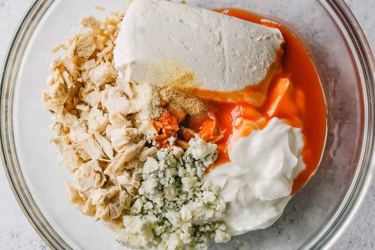 A bowl with ingredients for a Buffalo Chicken Dip with blue cheese and rotisserie chicken.