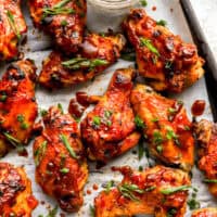 partial overhead view of crockpot chicken wings on a baking sheet with green onions.