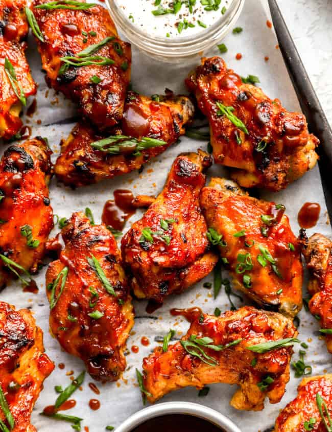 partial overhead view of crockpot chicken wings on a baking sheet with green onions.