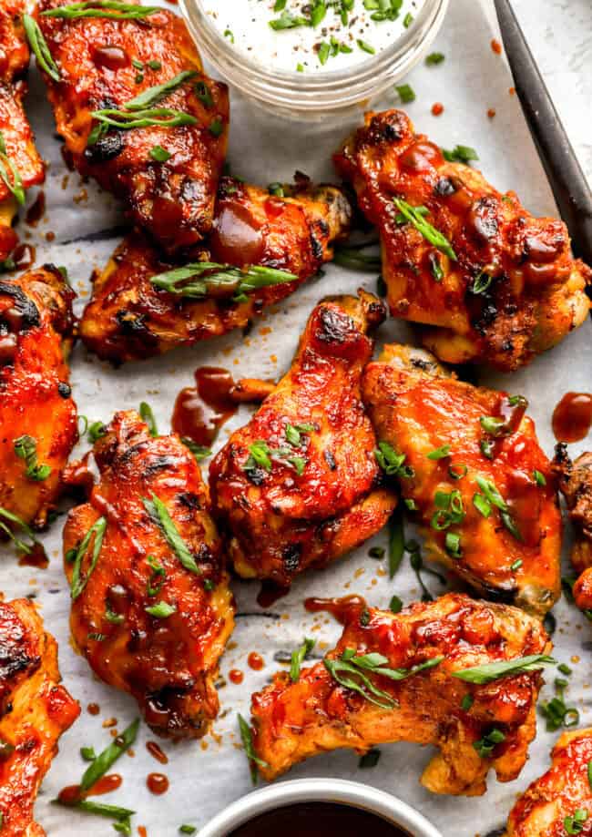 partial overhead view of crockpot chicken wings on a baking sheet with green onions.