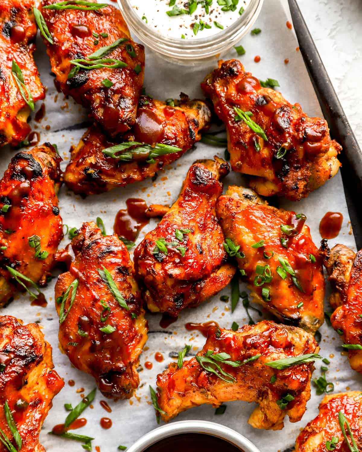 partial overhead view of crockpot chicken wings on a baking sheet with green onions.