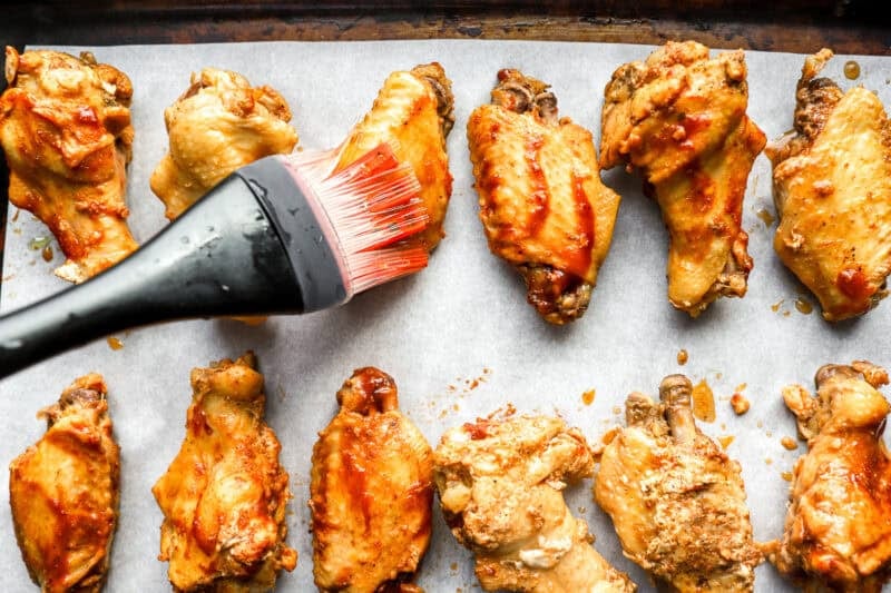 brushing chicken wings with oil on a baking sheet.