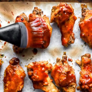 brushing chicken wings with bbq hot sauce on a baking sheet.