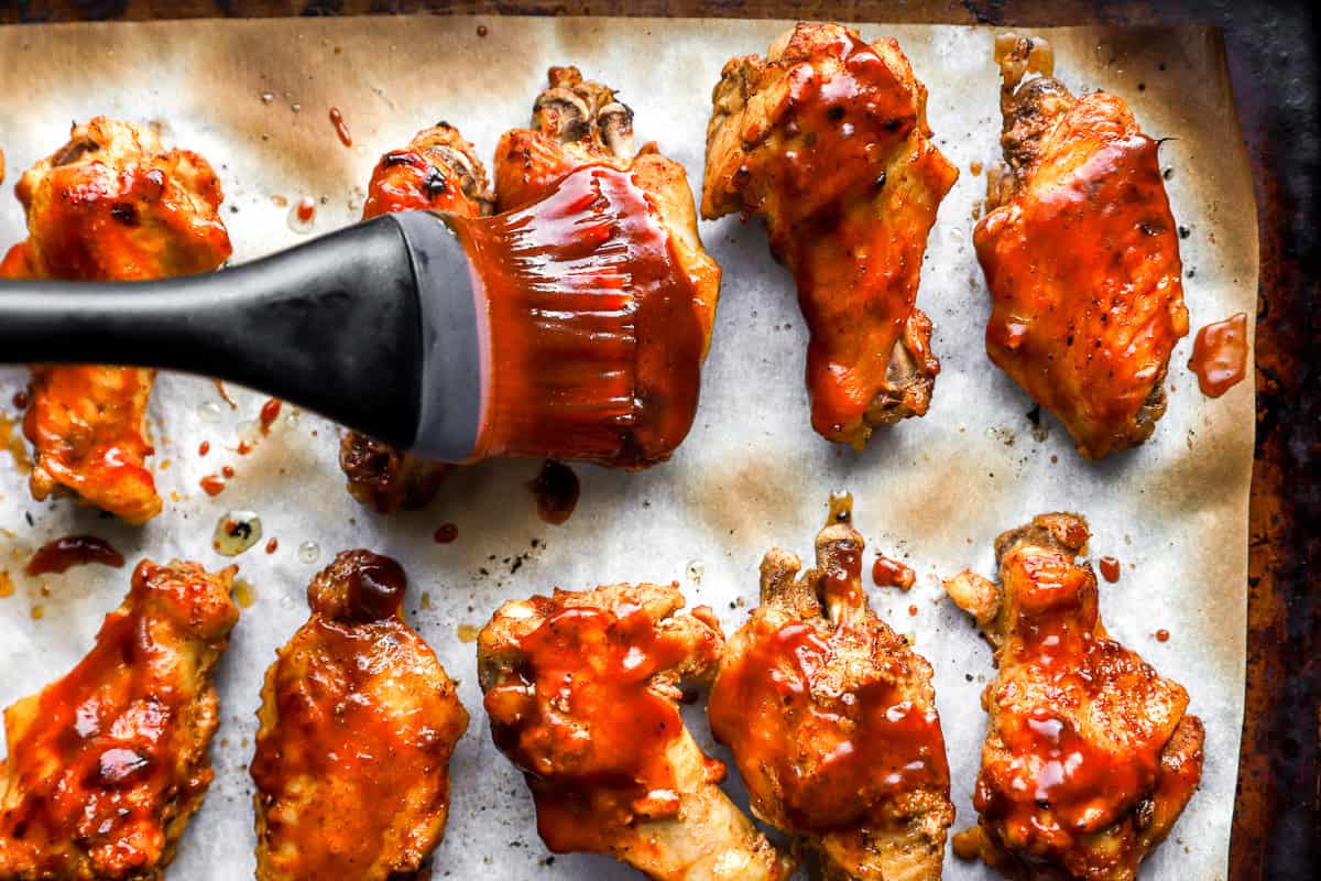 brushing chicken wings with bbq buffalo sauce on a baking sheet.