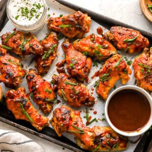 overhead view of crockpot chicken wings on a baking sheet with green onions and bowls of dipping sauce.