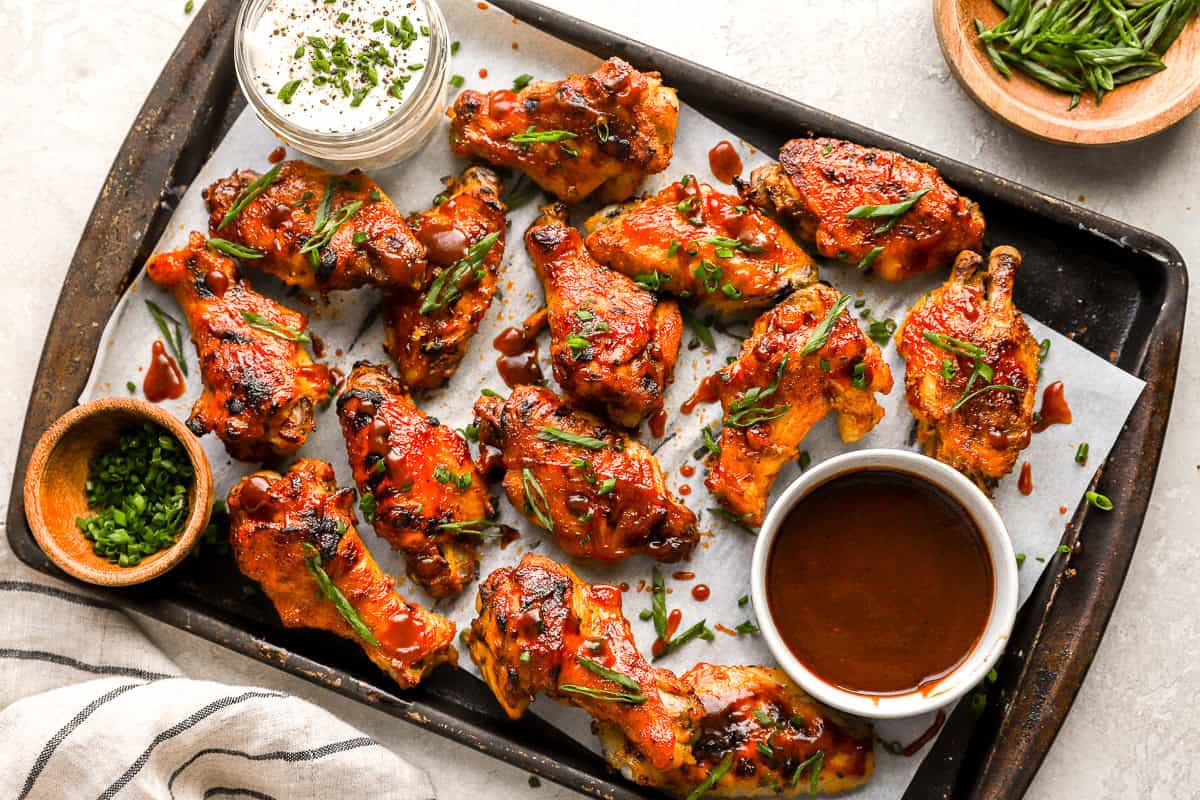 overhead view of slow cooker chicken wings on a baking sheet with green onions and bowls of dipping sauce.